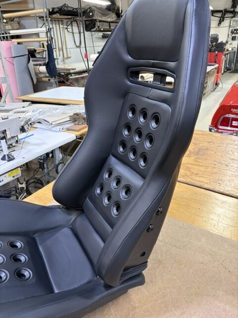 Side view of a performance seat recovered in black leather with perforated pads.