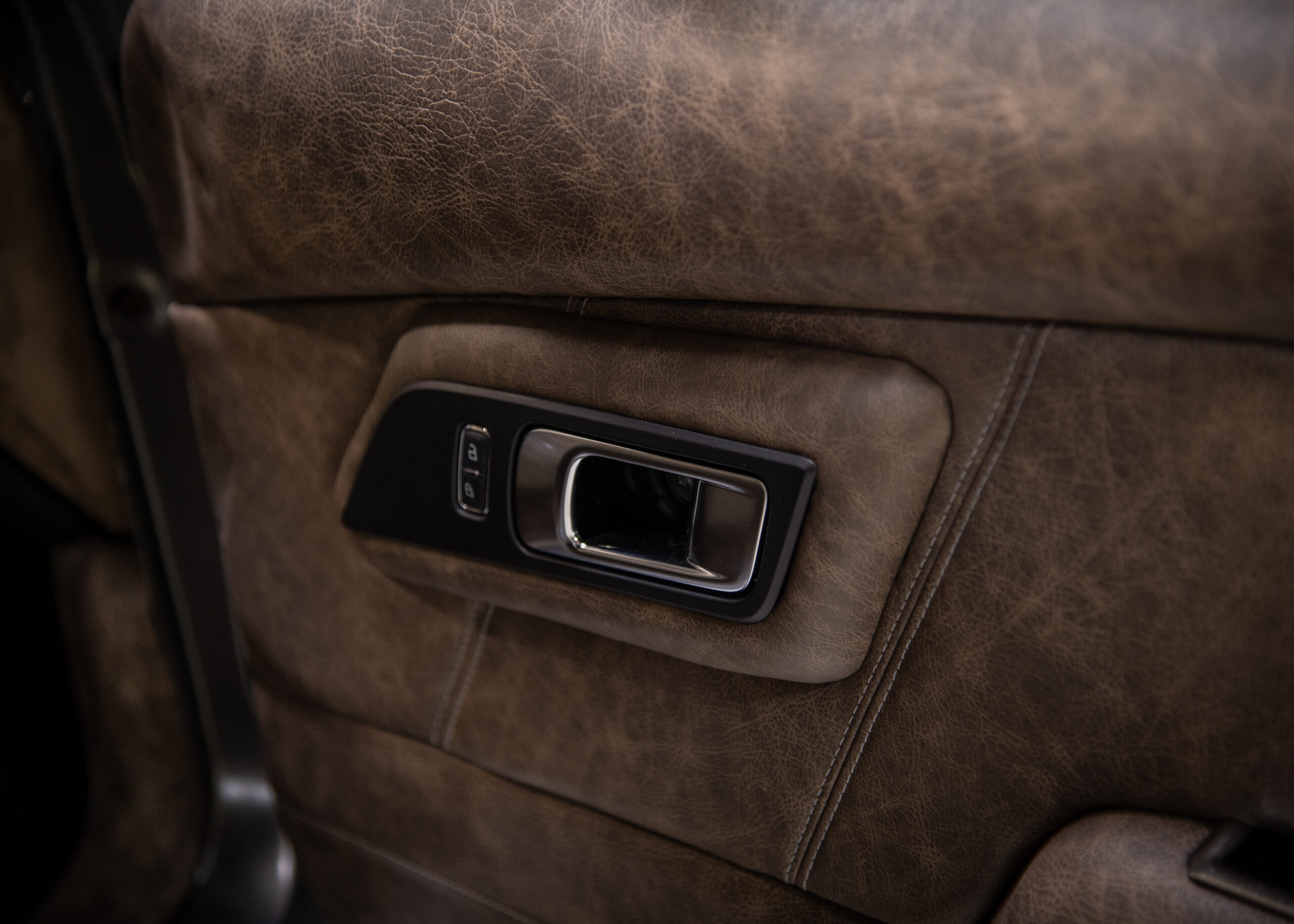 Close-up of a leather-covered door panel with stitch lines around the interior door handle.