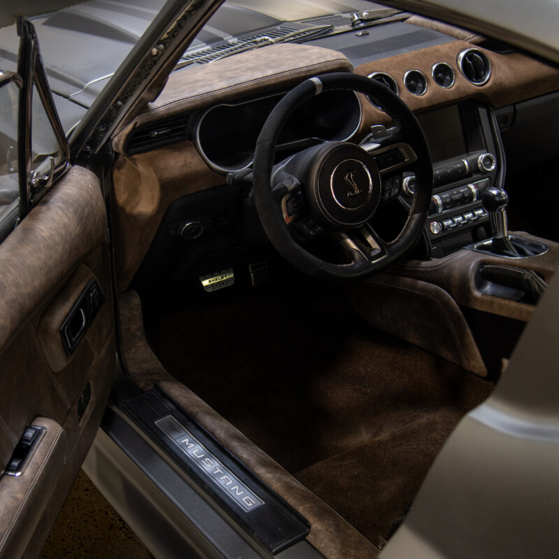 Driver-side view of a custom Shelby Mustang interior with a leather door panel, dashboard, center console, and carpet.