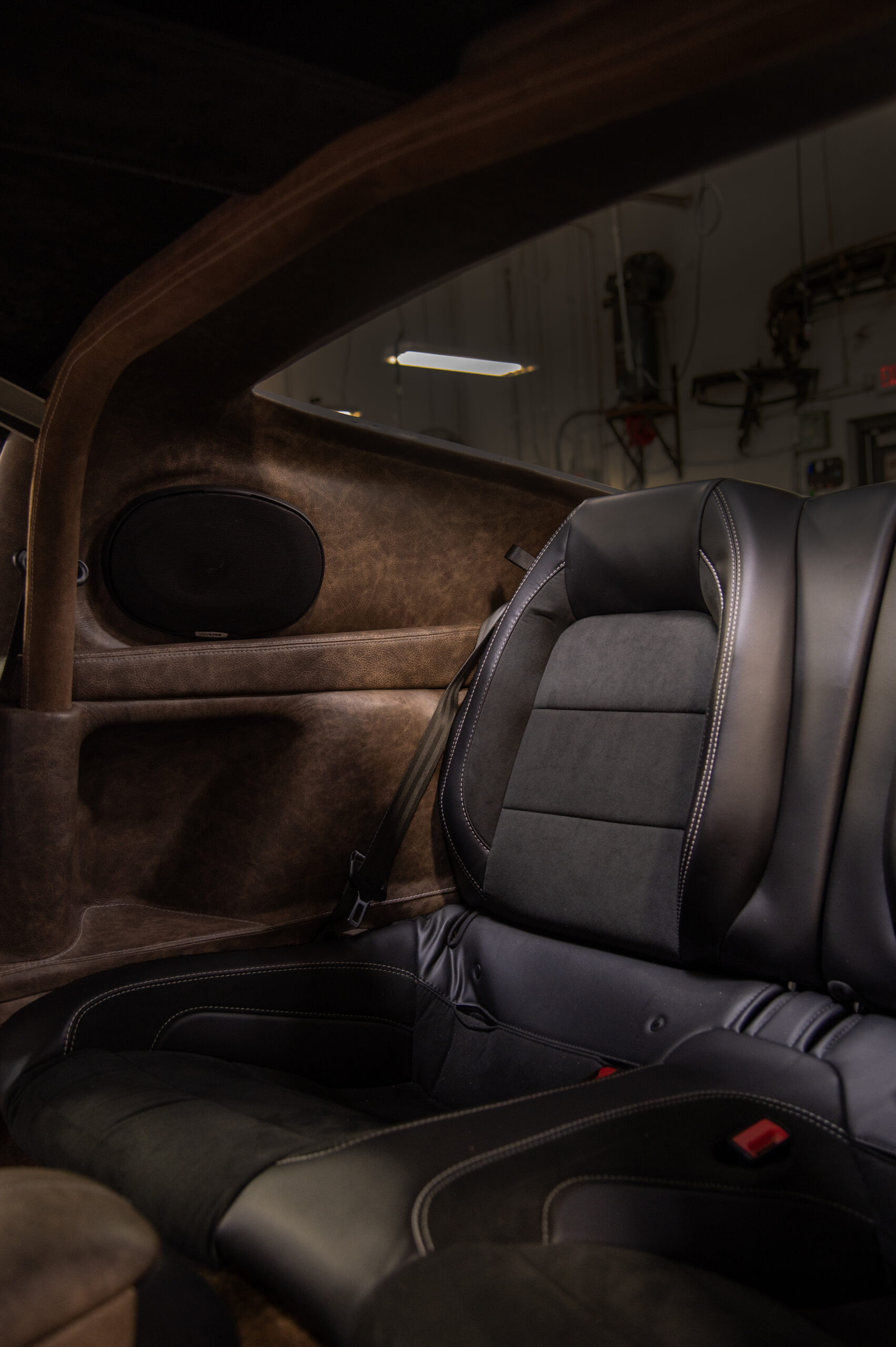 Rear seat in black leather and suede beside a rear quarter trim panel covered in brown leather.