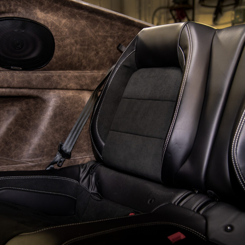 Black leather rear seat with contrast stitching beside a brown leather rear quarter trim panel.